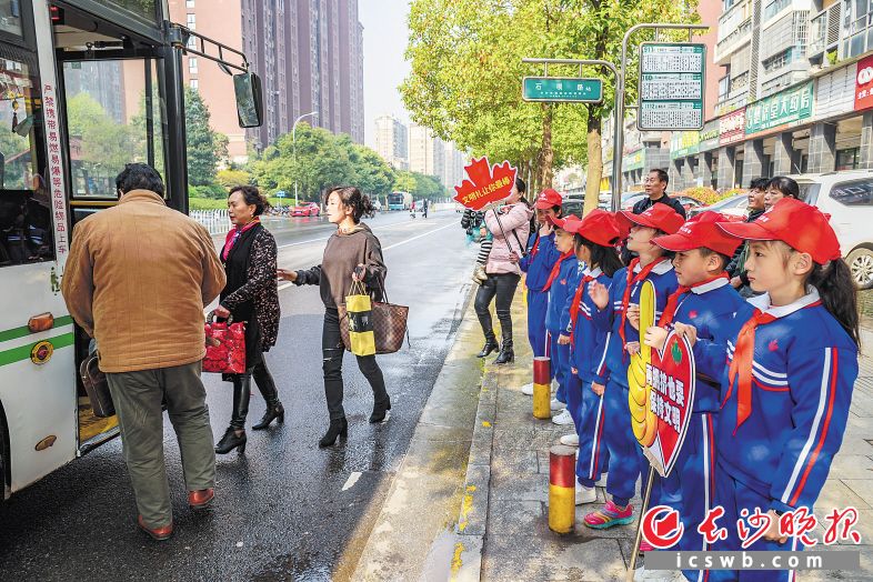 在长沙街头，处处可见排队礼让的文明场景。图为在雨花区石坝路公交站台边，来自枫树山大桥小学的孩子们举着排队礼让宣传牌，向市民宣传排队礼让。长沙晚报记者陈飞摄