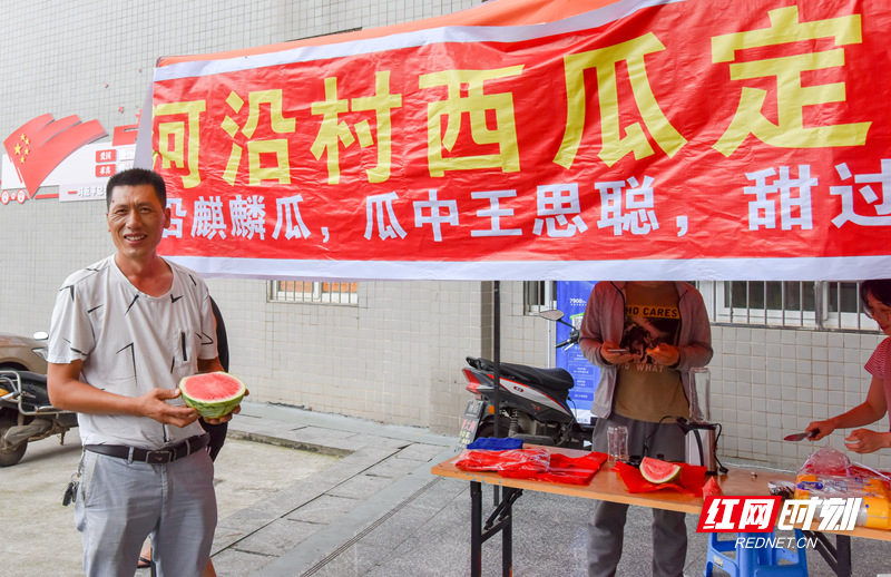 2019年6月14日上午，一辆小货车满载着省级扶贫点邵阳县小溪市乡河沿村的西瓜在该村对口帮扶单位邵阳学院教工餐厅卸货，原来通过网络扶贫商城——红小军商城预订西瓜的该校教师们纷纷前来挑选西瓜。前来送瓜的蔬果基地老板唐方华兴奋地手捧大红西瓜在扶贫单位帮忙搭建的售卖点前留影。.jpg