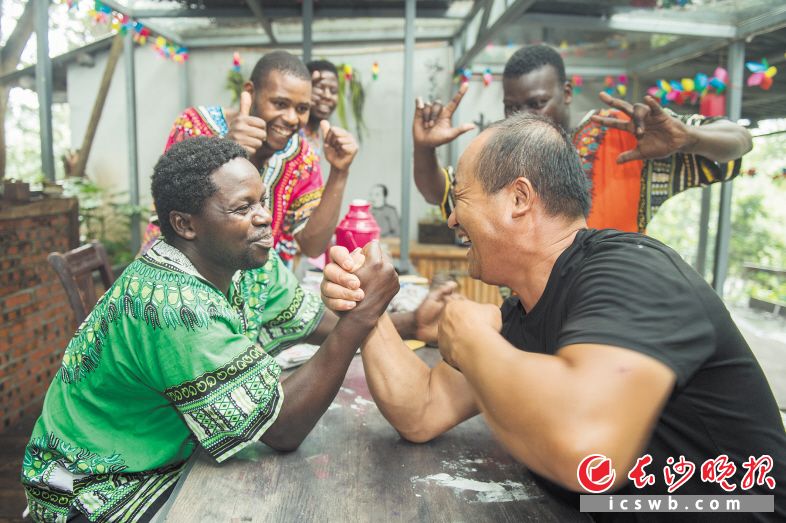 　　2019年6月21日，Tom在和中国朋友比赛扳手腕。来自乌干达的木雕艺人Tom是第二次来到河村非洲园，他和园内许多中国员工打成一片。