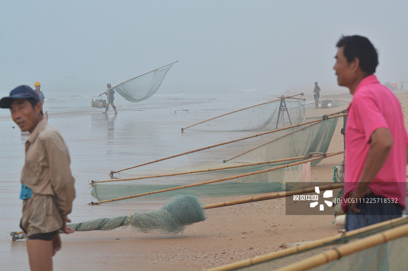 山东省日照海滨国家森林公园内的海边，一些早到的渔民站在海边休息。