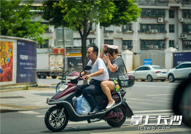 火炬路上，两位市民在高温下骑电动车，晒得有些受不了。