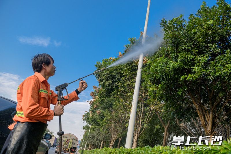 随车清洗员不仅对绿化带叶面积尘进行冲洗，还会同时清洗路灯杆、道路标识标牌等。