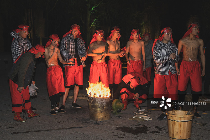 2019年1月1日，山东枣庄，台儿庄古城内的火龙钢花表演队的艺人们正光着膀子围在铁炉边取暖。
