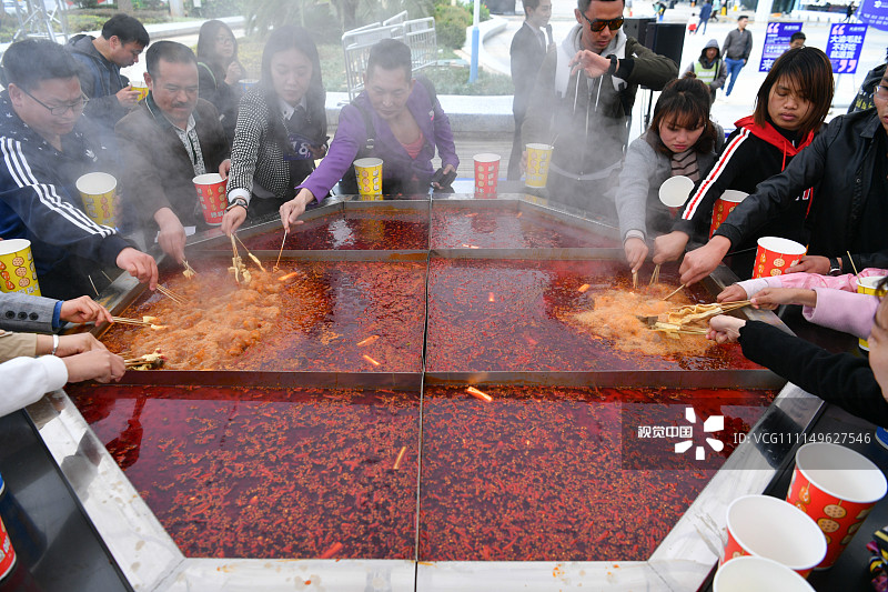 2018年4月6日，昆明，民众在直径3米的火锅前涮菜。当日，昆明街头一重庆火锅店举行“火锅宴”活动，在街头架设了直径3米的巨型火锅，并邀请民众参加比赛，现场品尝美味。
