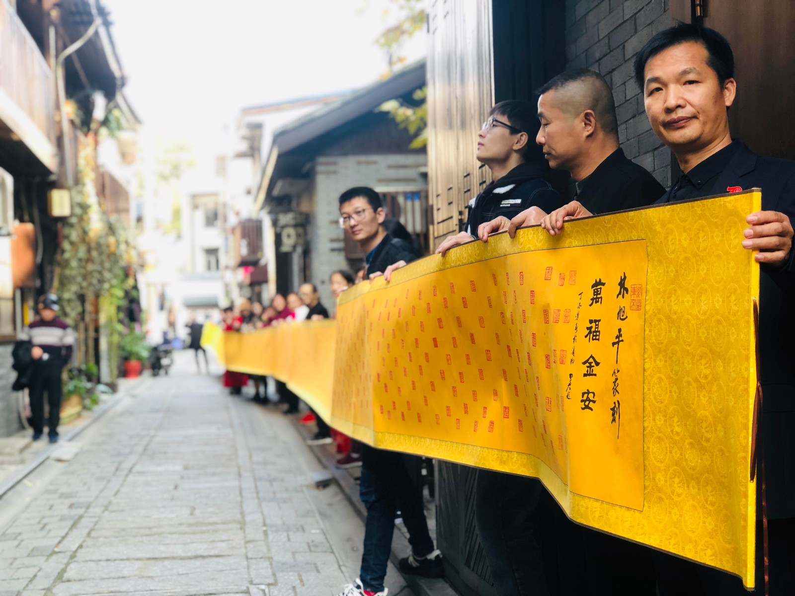 林旭平(右一)在幽深的古巷里展示30米长的6000篆刻福字长卷。 长沙晚报全媒体记者 李卓 摄