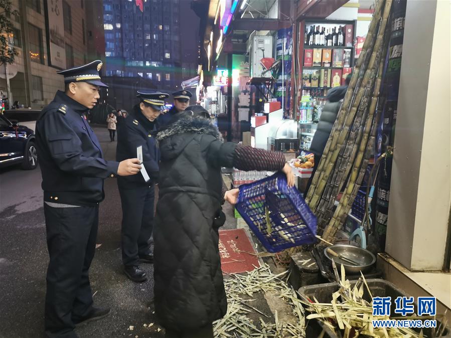 1月1日，城管队员围在街区一处水果店前，敦促店主收拾门前占道的甘蔗皮，以免影响人群疏散。 新华社记者 王昕怡 摄