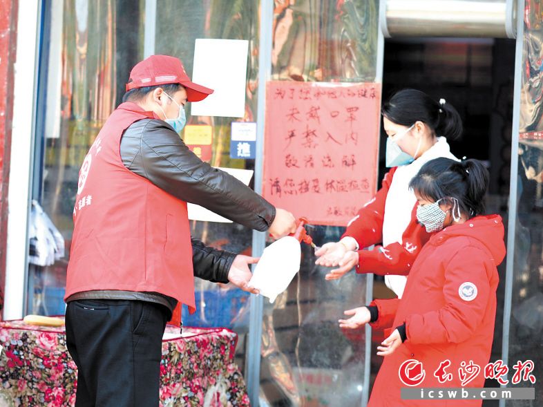 在喻家坳乡集镇的超市门前,志愿者为顾客消毒。黄苏 摄
