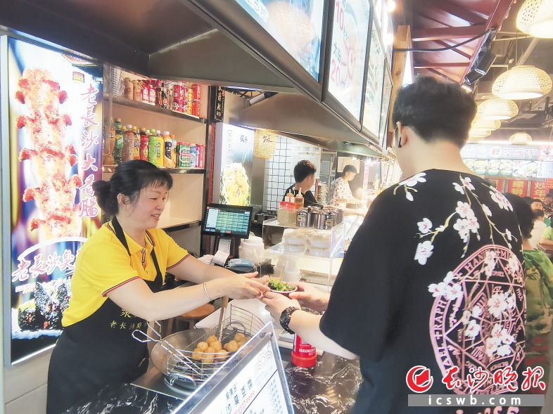 　　刘艳（左）向顾客端上自制臭豆腐。长沙晚报全媒体记者 王斌 摄