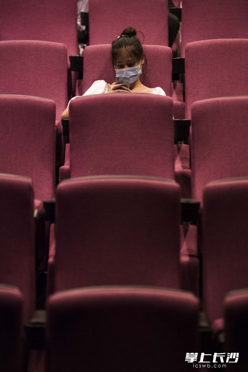 在放映厅电影放映开始前，一位女孩坐在玩手机。