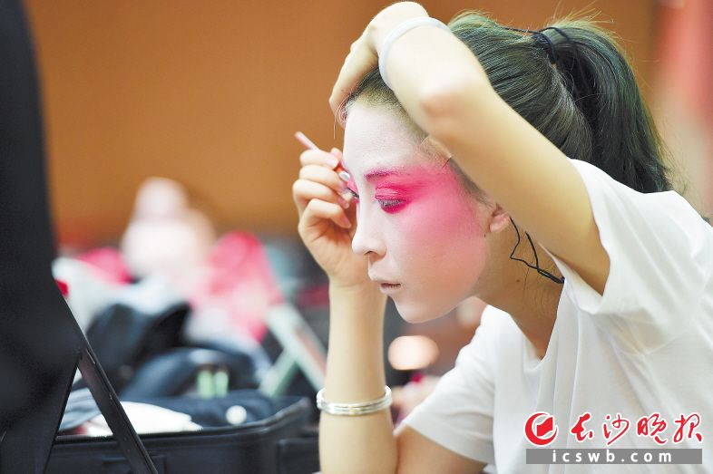 　　↑长沙市花鼓戏保护传承中心的青年演员吴乐茵在后台化妆，高温天气下，一脸的油彩使得演员相当难受。 