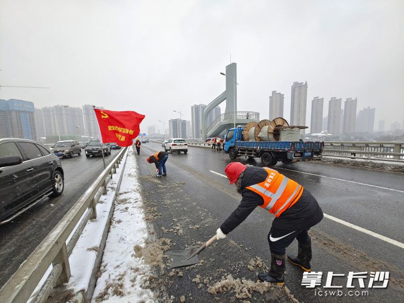 三汊磯大橋上，寒風(fēng)中飄揚(yáng)的紅旗和建筑工人志愿掃雪的身影，成了過往市民點(diǎn)贊的風(fēng)景。 長沙晚報(bào)全媒體記者 李卓 攝