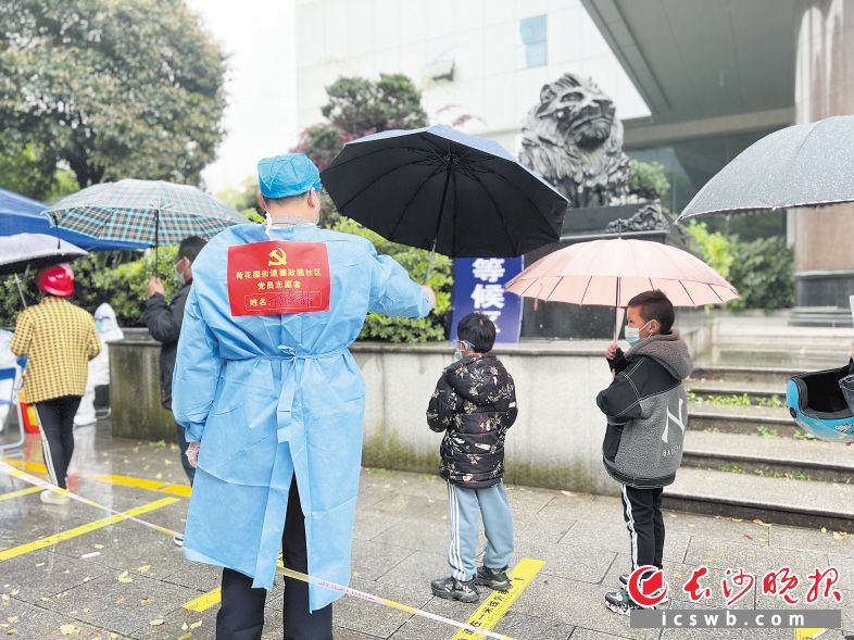 在芙蓉区德政园社区长沙房产交易大楼前坪核酸检测采样点,一个小男孩冒雨排队,党员志愿者胡景耀上前为他打伞,并与他保持着1米安全距离。长沙晚报通讯员 周淑 摄