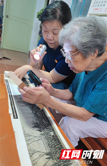 图片说明：94岁老党员屈仁慧，在用放大镜回看“传家宝”---与毛主席等中央领导人的合影。.png