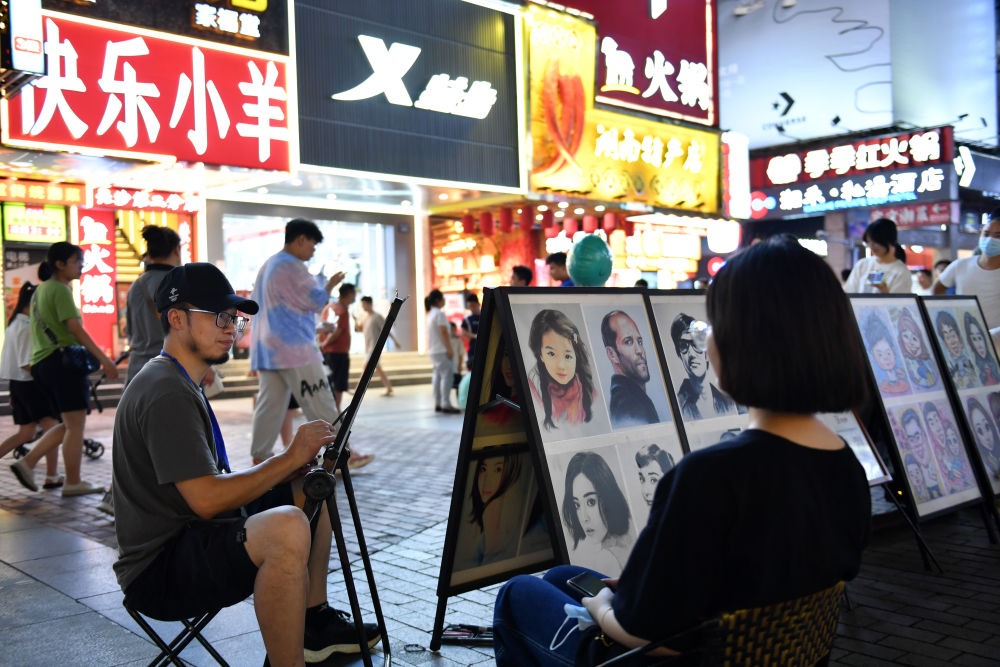 7月29日，在长沙市黄兴路步行街，一名画师（前左）为游客画像。