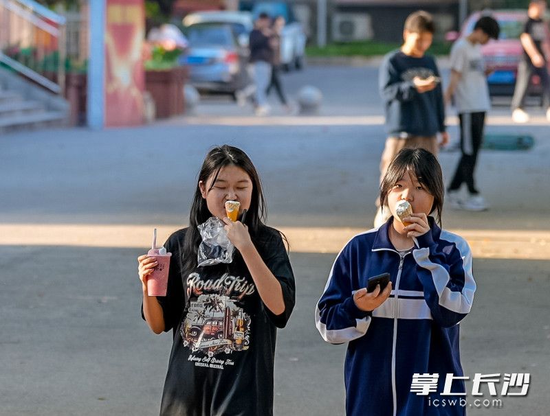 沐浴在暖阳下，两个女生边走边在吃冰淇淋。