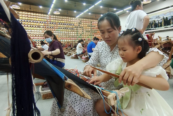 在“妈妈工坊”，从事织锦8年多的杨水莲在工余时间教5岁的女儿学习织锦。.jpg