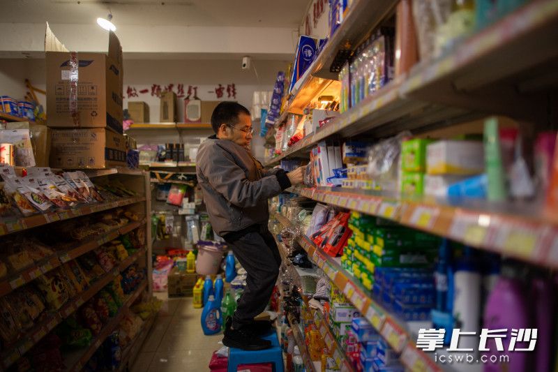 郭海波站在凳子上整理超市货架上的商品。