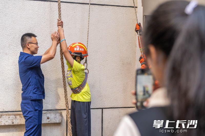 姐姐用手机记录下弟弟体验消防训练项目“攀绳”的过程。