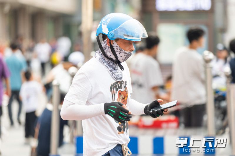 黄兴路步行街口，一位遮挡严实的快递小哥刚送完一单外卖。