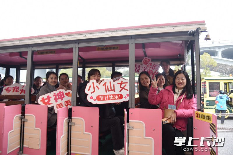 女性游客在粉色小火车上手持小道具合影留念。