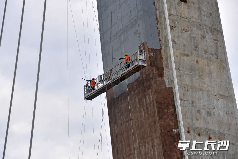百米高空，几位工人对主塔塔柱进行涂装。 