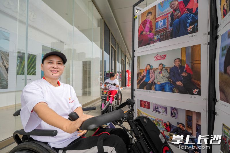 世界冠军李霞在轮椅上和影展里自己的照片“合影”。