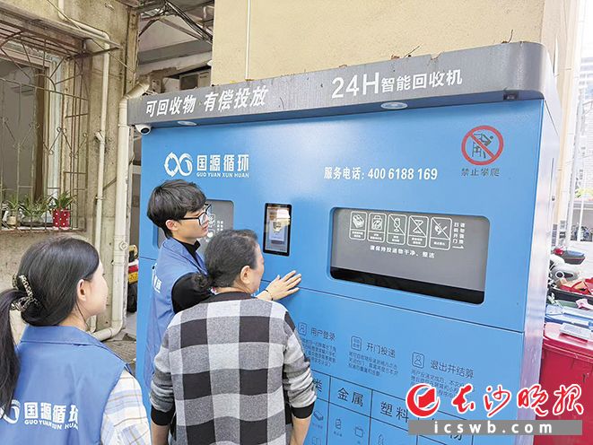 2026年，长沙城管实施“垃圾分类进楼栋”行动，在试点小区投放智能回收箱。这是垃圾分类志愿者向居民讲解垃圾分类标准与智能回收箱操作流程。                              市城管局供图